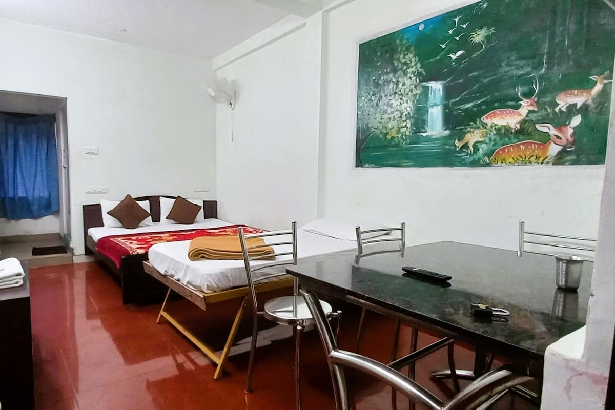 A hotel room with a bed, a dining table with chairs, a painting of deer on the wall, and a door with a handle.