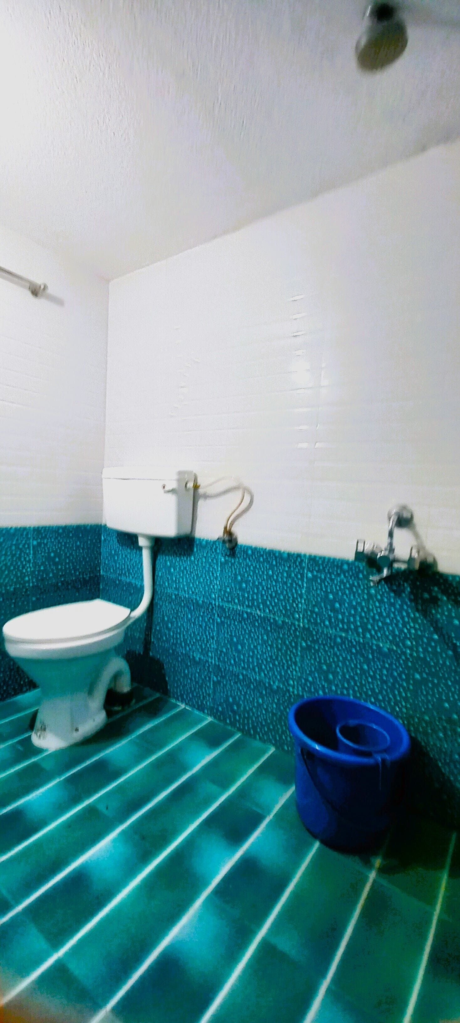 Un baño con un inodoro blanco, un cubo azul y una pared con azulejos azules.