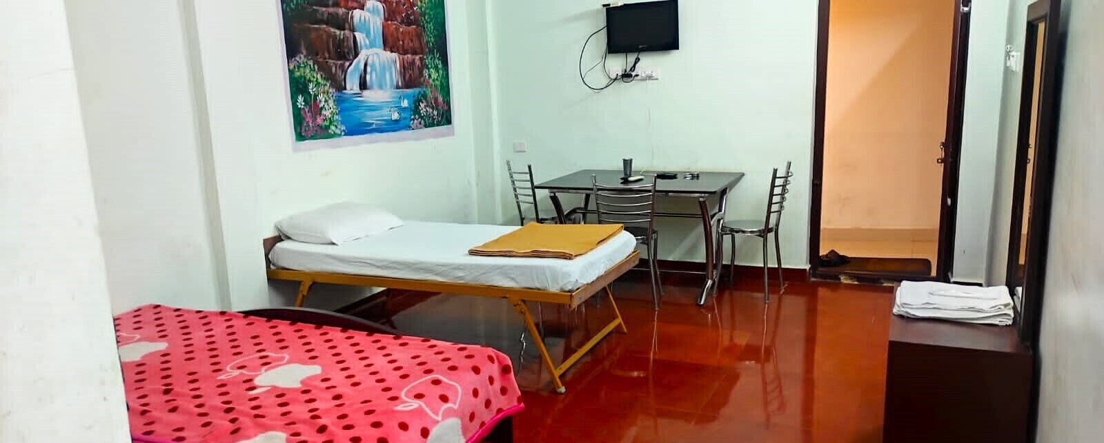 Una habitación pequeña con una cama, un escritorio y una silla. Hay un cuadro en la pared y un televisor sobre el escritorio.