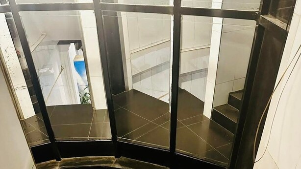 A staircase with dark tiles and glass panels, leading to a landing with white walls and a visible door. - Triple H Hotel  (Yangon)