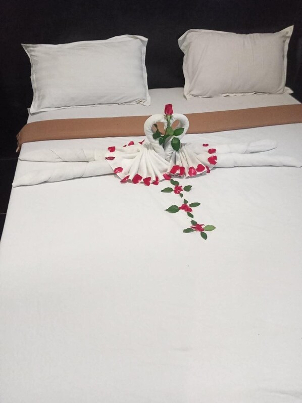 A neatly made bed with white linens, a brown bedspread, and a decorative towel arrangement featuring a rose and leaves. - Triple H Hotel (Yangon)