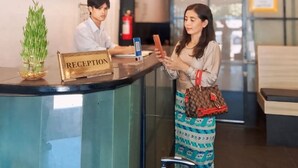 A reception desk with a sign reading "RECEPTION," a potted plant, and a fire extinguisher in the background. - Triple H Hotel  (Yangon)