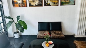 A room with a black leather sofa, a black coffee table with fruit and flowers, and four framed paintings on the wall. - Triple H Hotel  (Yangon)