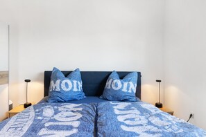 Una cama con ropa de cama y almohadas azules, dos lámparas de noche y un enchufe en la pared.
