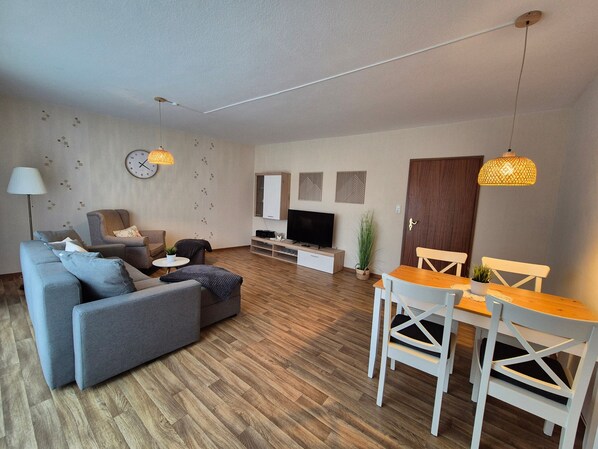 A modern living room with a sofa, TV, dining table, and chairs.