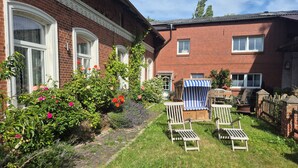 Une maison en briques avec un jardin, un espace extérieur aménagé pour s’asseoir et un petit abri de jardin.