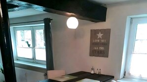 Un coin repas avec une table en bois, des chaises blanches, un luminaire suspendu, une fenêtre avec des rideaux et un mur orné d’une citation inspirante.