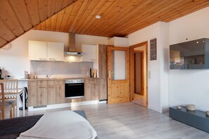 A modern kitchen with wooden cabinets, a built-in oven, and a dining area with a chair and table. - Apartment 'Steinhart' with Balcony and Wi-Fi (Lenzkirch)