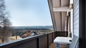 Un balcon donnant sur un paysage boisé, avec une table et une chaise.