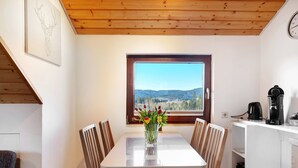 Un coin repas comprenant une table, des chaises, un vase avec des fleurs, une fenêtre donnant sur un beau paysage et une machine à café.