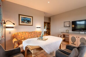 Une pièce chaleureuse avec un canapé à motifs, une petite table sur laquelle est posée une bougie, un téléviseur et un tableau encadré accroché au mur.