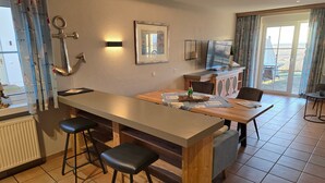 A modern kitchen with a central island, bar stools, a dining table, and a view of the outdoors. - Apartment 'Seeschwalbe' with Sea View, Shared Terrace and Wi-Fi (Mönchgut)