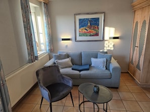 Een woonkamer met een grijze bank, een zwarte fauteuil, een klein rond tafeltje en een schilderij aan de muur.