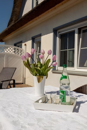 Een witte tafel met een dienblad waarop een waterfles, een glas en een bloeiende plant met roze bloemen staan.