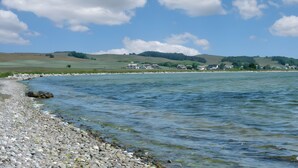 A calm lake with a pebble beach, houses in the background, and a clear sky. - Apartment 'Seeschwalbe' with Sea View, Shared Terrace and Wi-Fi (Mönchgut)
