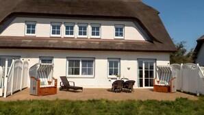 A house with a large thatched roof, white exterior walls, multiple windows, and a patio area with outdoor furniture. - Apartment 'Seeschwalbe' with Sea View, Shared Terrace and Wi-Fi (Mönchgut)