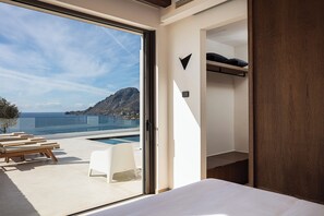 A modern hotel room with a large sliding glass door leading to a balcony with a pool and a mountain view. - Rokkea Villa, Earthy Elegance by the Sea (Rethymno)