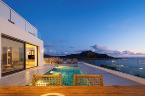 Un espace piscine extérieur moderne avec vue sur la mer, des chaises longues et une table en bois.