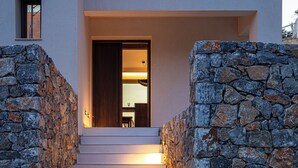 A modern building with a stone wall and a staircase leading to a wooden door.