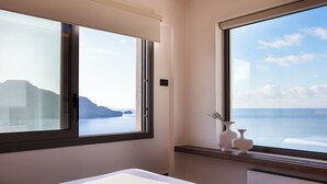 A hotel room with a bed, two windows, and a view of the sea and mountains.