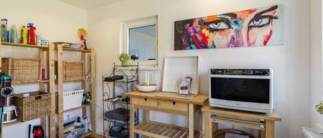 A room with a wooden shelf unit, a microwave, a painting, and a window.
