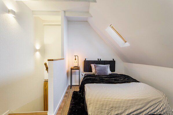 Ein Schlafzimmer mit einem Bett, einem Nachttisch, einer Lampe, einem Fenster und einer Treppe.