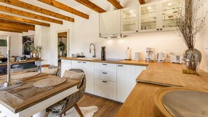 Una cocina moderna con vigas de madera, armarios blancos y un comedor con mesa y sillas de madera.