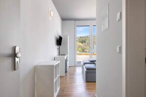 A modern room with a wooden floor, a white wardrobe, a television, and a view of the outdoors.