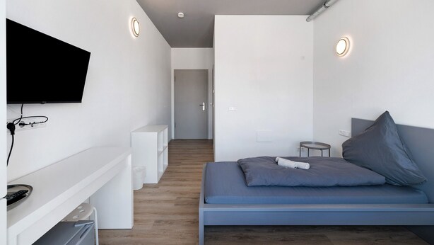 Een moderne slaapkamer met een bed, een aan de muur bevestigde televisie en een gang die naar een andere kamer leidt.
