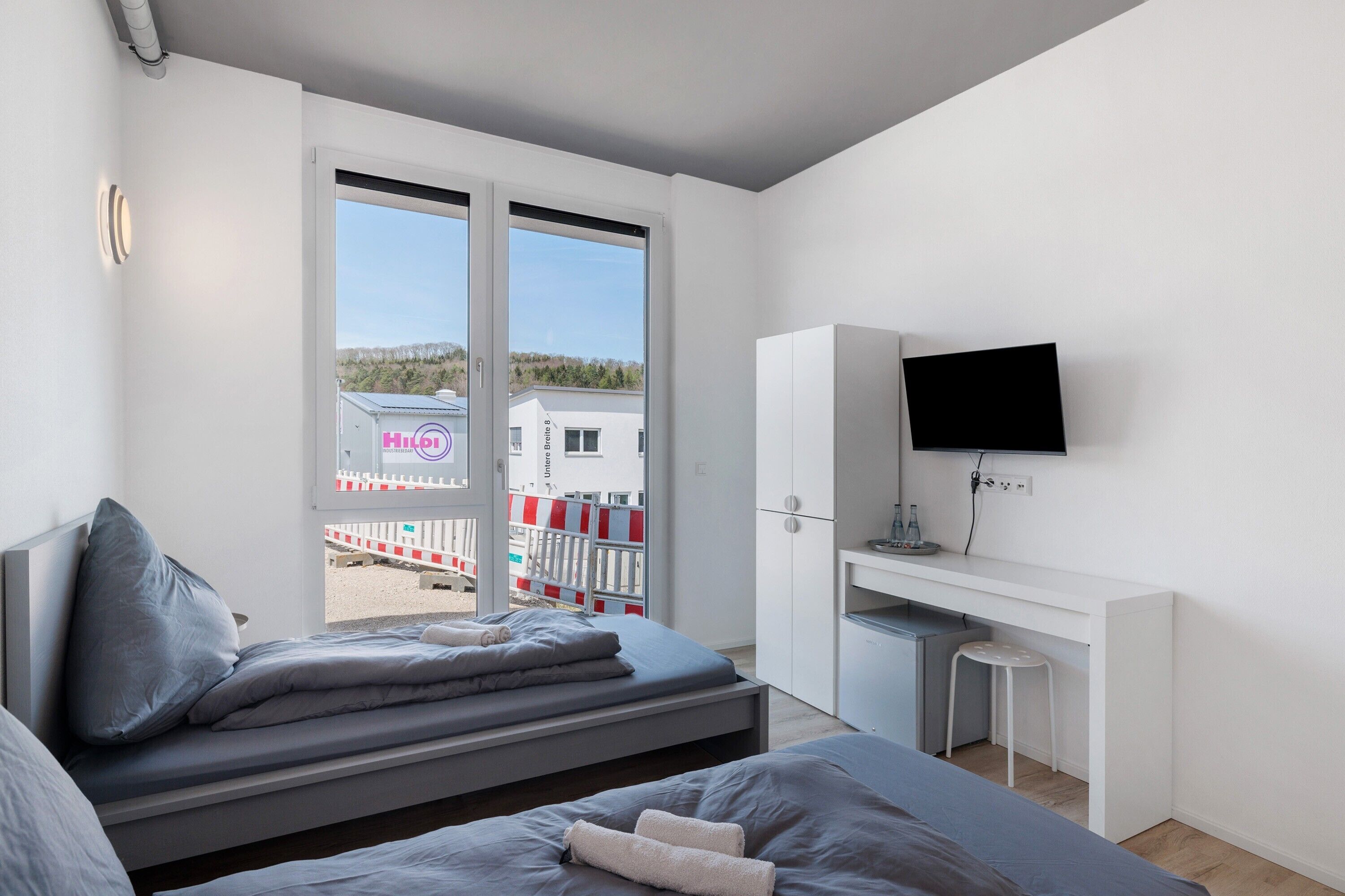 A modern hotel room with a bed, a desk, a TV, and a view of the outside.