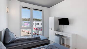 A modern hotel room with a bed, a desk, a TV, and a view of the outside.