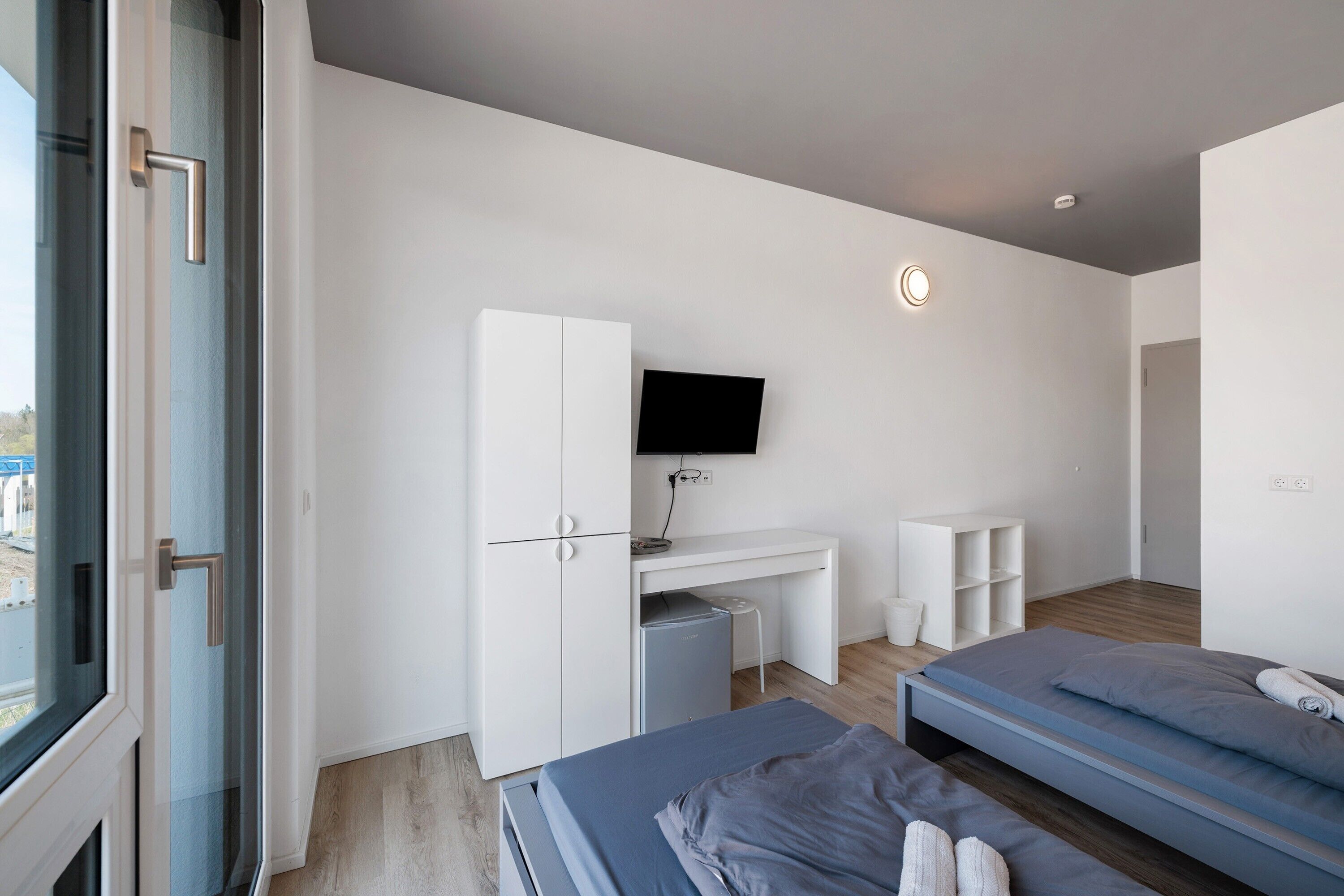 A modern bedroom with a bed, desk, and TV.