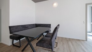 Een moderne kamer met een donkere bank en stoel, een licht houten vloer en een plafondlamp.
