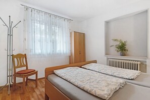 Un dormitorio con cama de madera, una silla, un radiador y una ventana con cortinas translúcidas.