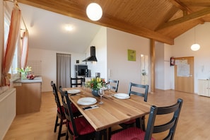 Un comedor con una mesa de madera, sillas y una cocina al fondo.