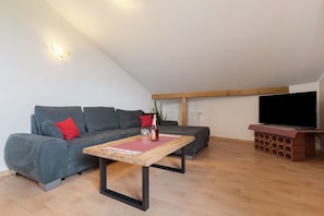 Un salon moderne avec un canapé gris, une table basse en bois, un téléviseur à écran plat et un meuble TV dont le motif rappelle celui d’un mur en briques.
