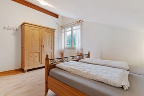 Un dormitorio con cama de madera, un armario, una ventana con cortinas y un radiador.