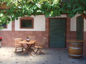 Un patio al aire libre con una mesa y sillas de madera, una botella de vino y un barril.