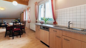 Cuina amb armaris de fusta, rentaplats integrat, taulell de granat i finestra amb cortines.
