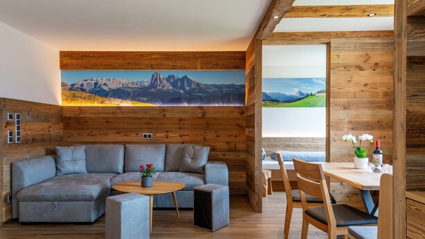 A modern living room with a wooden interior, a large sofa, a small table, and a dining area with wooden chairs.