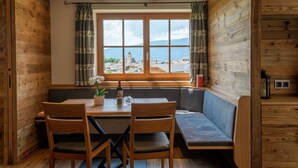 A wooden-paneled room with a dining table, chairs, and a bench. A window offers a view of a town and mountains.