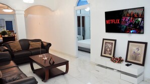 A living room with a black leather sofa, a wooden coffee table, and a white TV mounted on the wall displaying Netflix content.