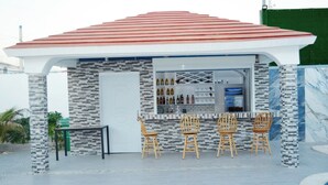 A small outdoor bar area with a tiled floor, a red roof, and a brick wall. There are four wooden chairs and a small table.