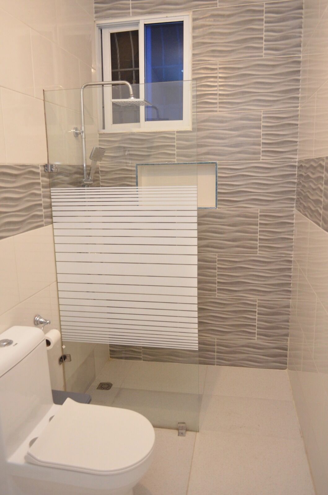 Ein Badezimmer mit Toilette, einer Dusche mit Glastrennwand und einem Fenster über der Dusche.