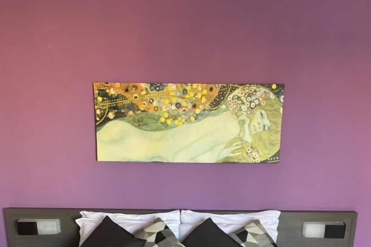 A bed with a patterned bedspread, two nightstands, and a painting on the wall.