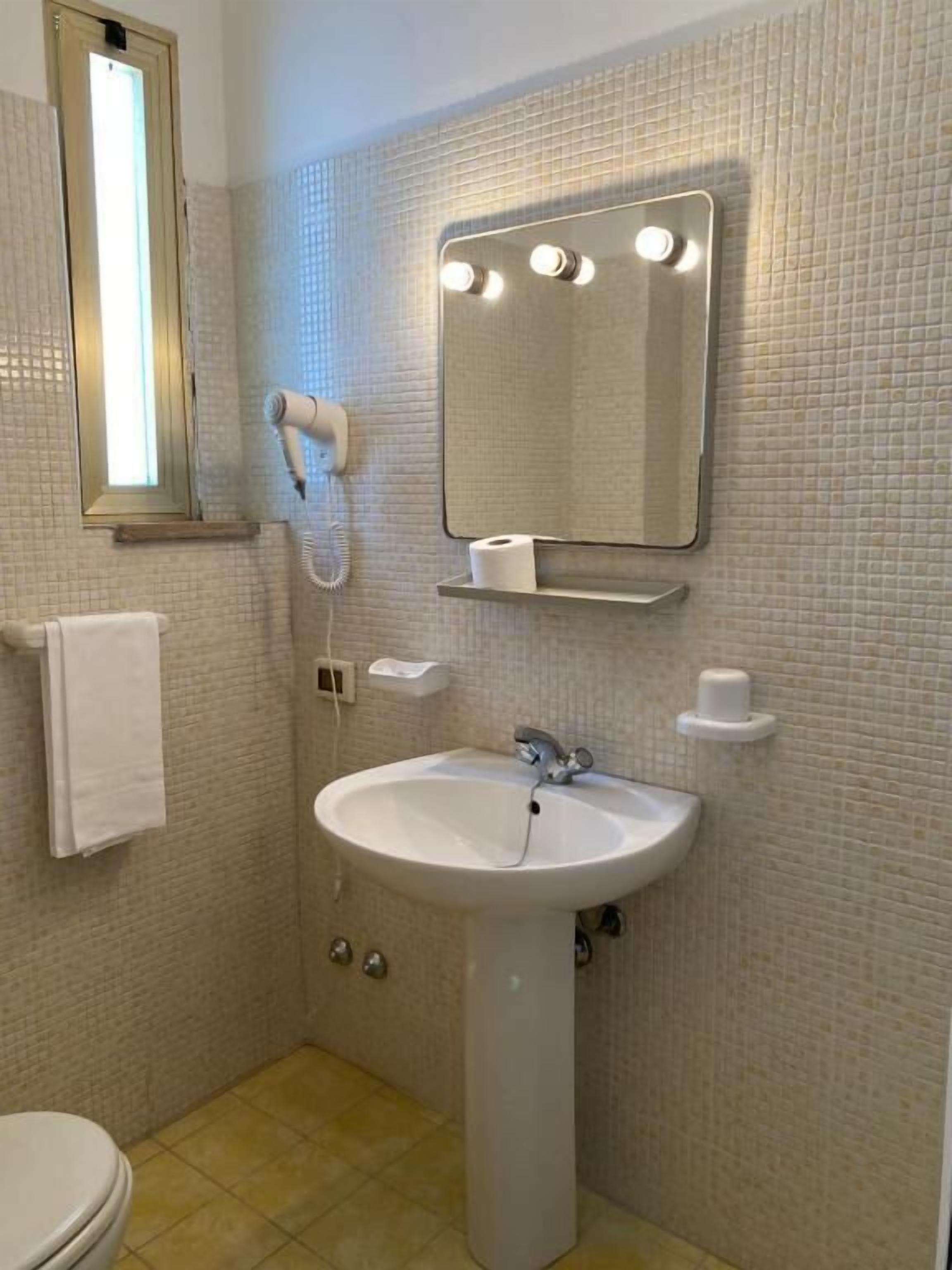 A bathroom with a white sink, a mirror with lights, a hairdryer, and a towel rack.