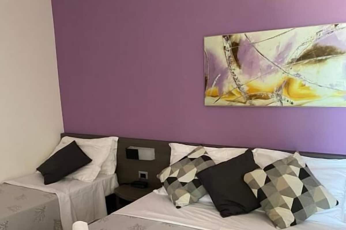 A hotel room with two beds, each with a patterned bedspread, a headboard, and multiple pillows. There is a painting on the wall above the beds.