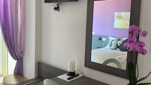 A hotel room with a desk, chair, TV, air conditioning unit, and a potted orchid. - Hotel Spiaggia D'Oro (Mondolfo)