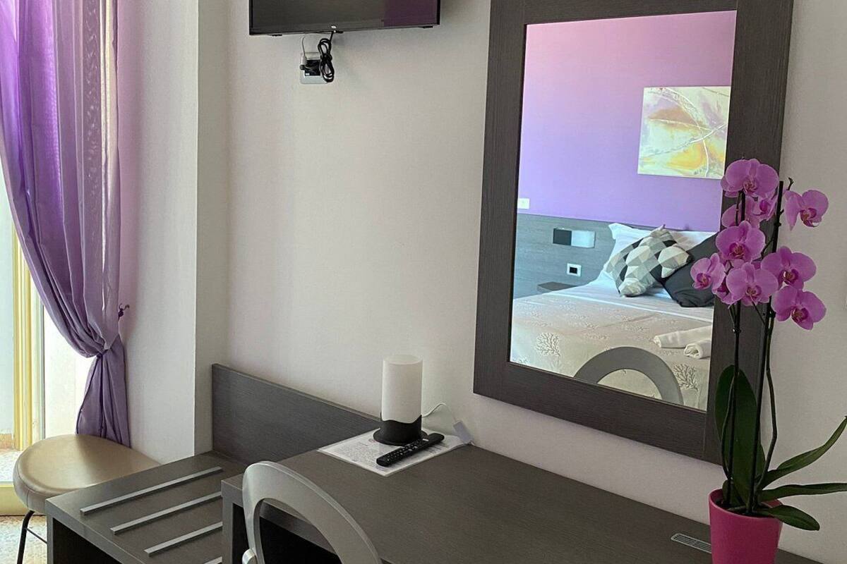A hotel room with a desk, chair, TV, air conditioning unit, and a potted orchid.
