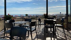An outdoor seating area with tables and chairs, overlooking a beach with umbrellas and a clear sky. - Hotel Spiaggia D'Oro (Mondolfo)